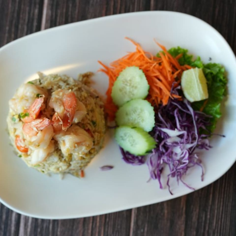 Blai Thai shrimp fried rice with shredded carrots, red cabbage, cucumber slices, and lime.
