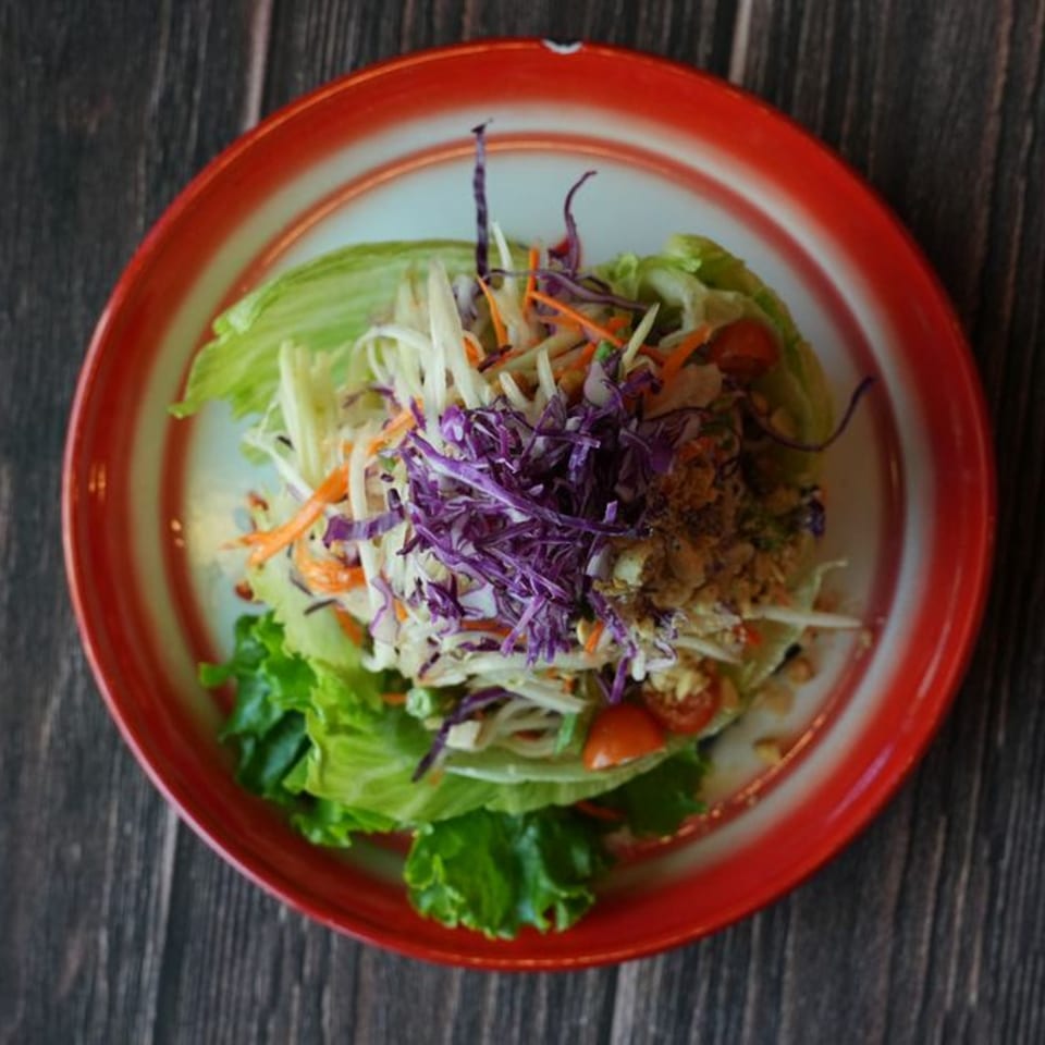 Overhead view of a vibrant Thai salad with lettuce, shredded cabbage, carrots, and cherry tomatoes.