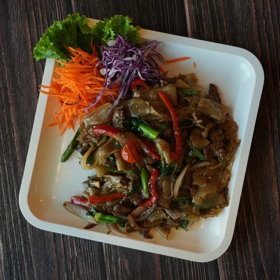 Thai Drunken Noodles with beef, red peppers, and green vegetables, garnished with shredded carrots and cabbage.
