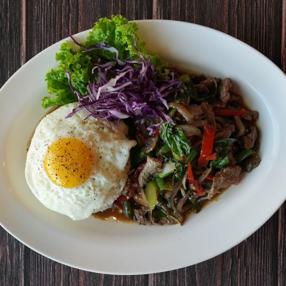 Blai Thai's stir-fried beef with vegetables and a fried egg, served on a white plate.